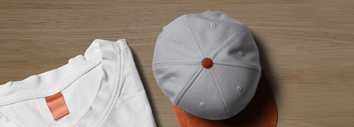 A white t-shirt and a grey cap on a wooden table.