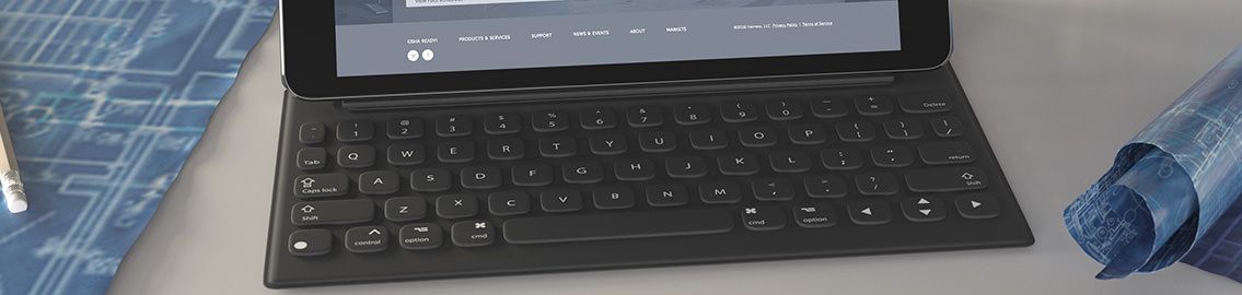 Bottom of a tablet demonstrating the app, a tablet keyboard and various background blueprints.