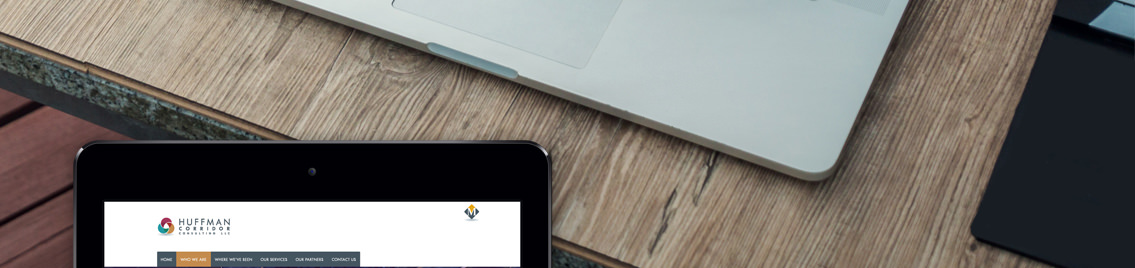 Laptop, wooden table and mobile device displaying Huffman Corridor Consulting website.