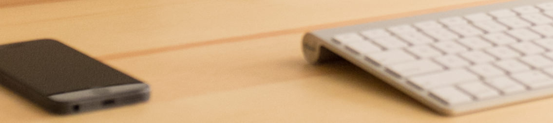 Keyboard and mobile device resting on a wooden desk.