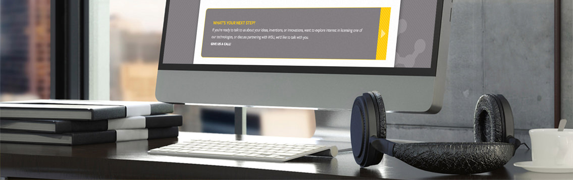 A desk, headphones and office paraphernalia, as well as the bottom of a monitor displaying WSU Ventures’ website.
