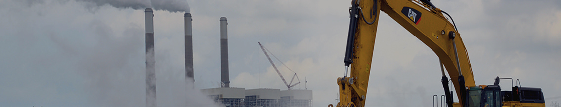 Yellow CAT machine in foreground with smoke stacks in background.